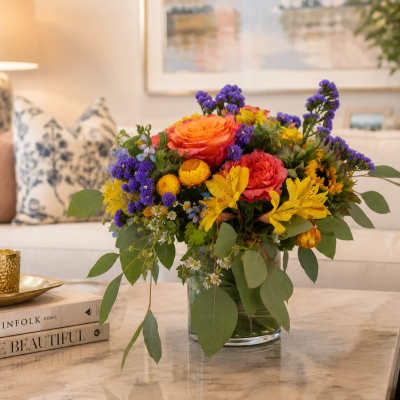 Mixed bouquet of orange, pink, yellow, and purple flowers in a glass vase