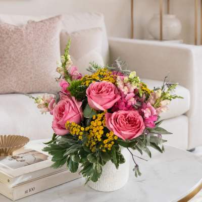 Pink roses and yellow filler flowers in a white vase on a coffee table