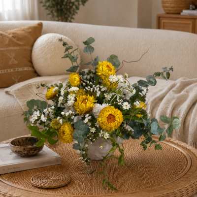 Yellow and white flower arrangement in a white vase on a woven coffee table