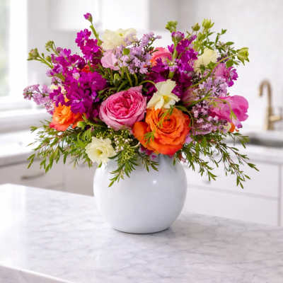 Mixed pink, orange, and white flowers arranged in a white vase