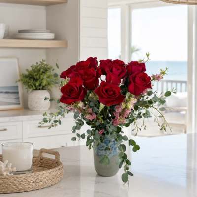 Red roses arranged in a ceramic vase with pink filler flowers