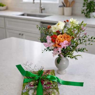 Small mixed flower arrangement in a white vase beside a ribbon-tied book