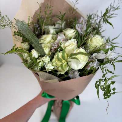Bouquet of white roses with greenery wrapped in brown paper and tied with a green ribbon