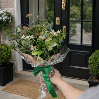 Handheld bouquet of mixed white and pale pink flowers wrapped in clear plastic with a green ribbon