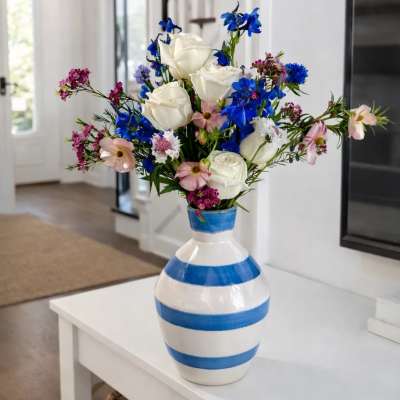 Bouquet of white roses, blue flowers, and pink blooms in a striped ceramic vase