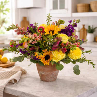 Colorful mixed flower arrangement in a terracotta pot on a kitchen counter