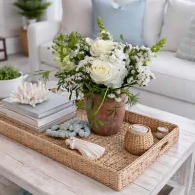 White rose arrangement in a rustic vase on a woven tray