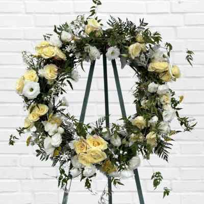 Circular floral wreath with pale yellow and white roses on a stand