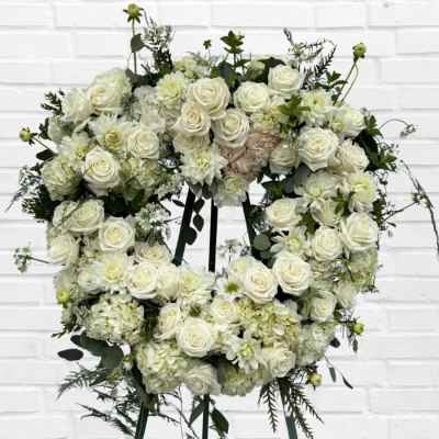 Heart-shaped wreath of white roses and pale blooms on a stand