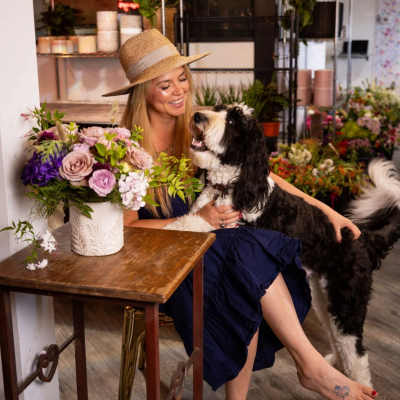 Woman holding a dog beside a vase of pink and purple flowers