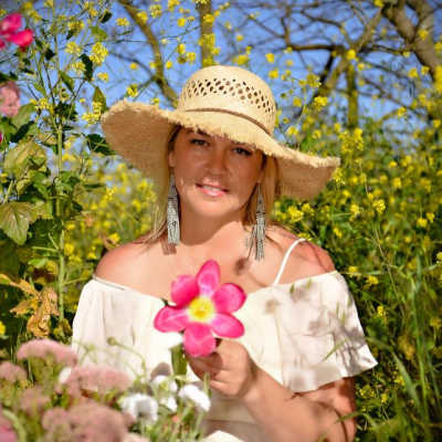 Woman in a straw hat holding a pink flower in a field of yellow blooms