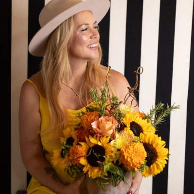 Woman holding a bouquet of sunflowers and orange flowers in a vase
