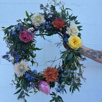 Circular floral wreath with roses, dahlias, and blue flowers