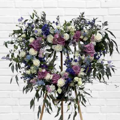 Heart-shaped floral wreath with purple and white roses on a stand