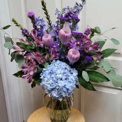 Bouquet of blue hydrangea, purple flowers, and pink alstroemeria in a glass vase