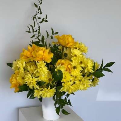 Yellow flowers arranged in a white vase with dark green foliage