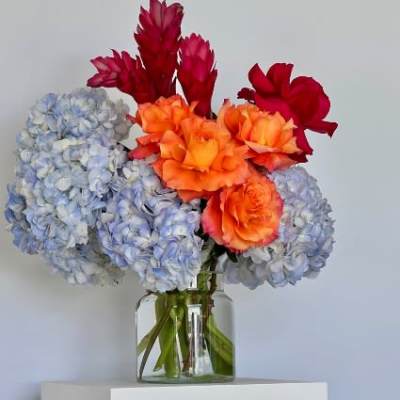 Bouquet of blue hydrangeas and orange-red flowers in a glass vase