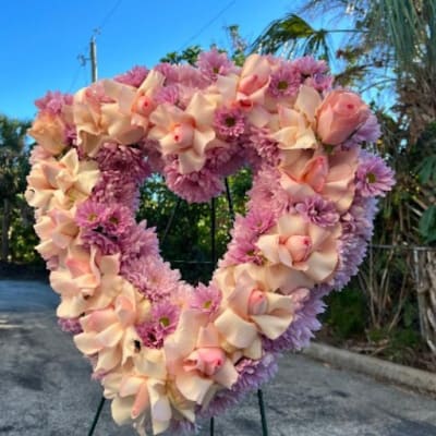 Heart-shaped floral wreath with pink and peach blooms on a stand