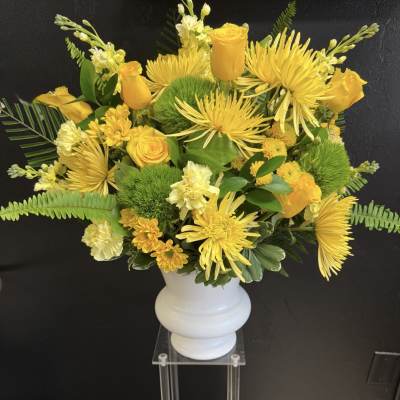 Yellow floral arrangement in a white vase with roses and spider mums