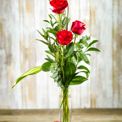 Red roses in a tall clear vase with scattered heart confetti