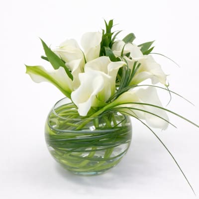 White calla lilies arranged in a round glass vase