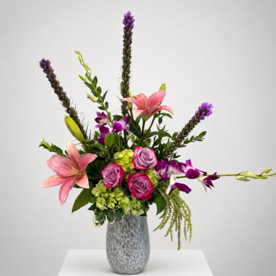 Pink lilies and roses in a gray vase with purple orchids