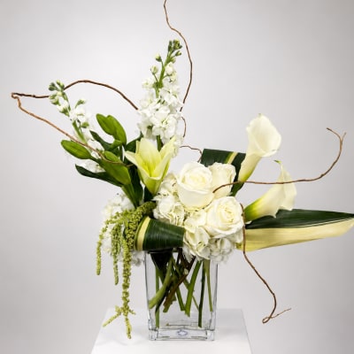 White roses, calla lilies, and orchids in a clear glass vase