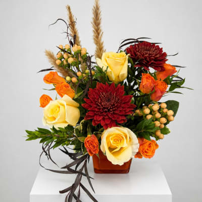 Arrangement of yellow and orange roses with red chrysanthemums in a square vase