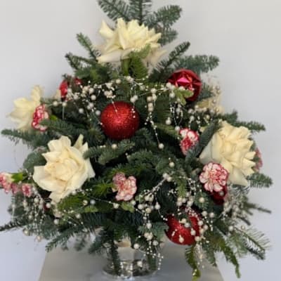 Christmas arrangement with white flowers, red ornaments, and evergreen branches in a glass vase