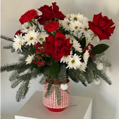 Red roses and white daisies in a red-and-white vase with evergreen branches