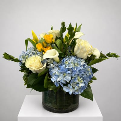 Blue hydrangeas with white roses and yellow calla lilies in a glass vase