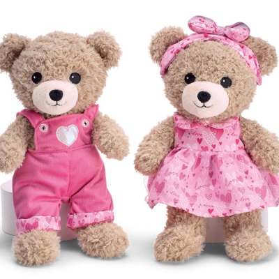 Two teddy bears in pink outfits, one in overalls and one in a dress