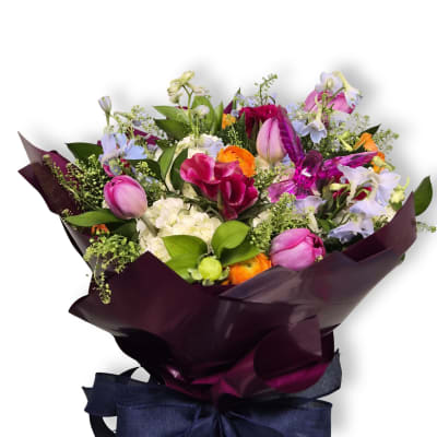 Mixed bouquet of pink tulips, orange ranunculus, and pale flowers wrapped in dark paper