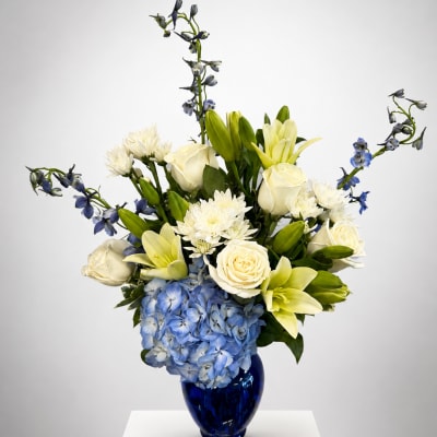 Blue hydrangeas, white roses, lilies, and blue delphinium in a cobalt vase
