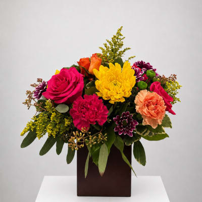 Colorful mixed bouquet in a dark square vase with roses, carnations, and chrysanthemums