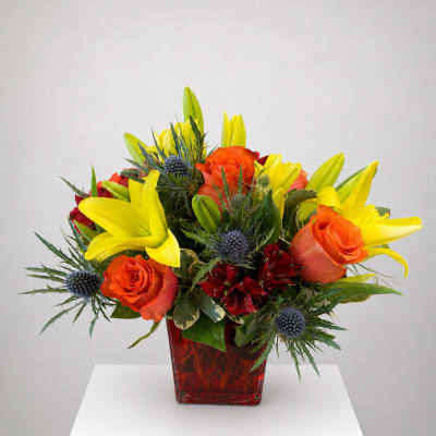 Orange roses and yellow lilies in a red glass vase