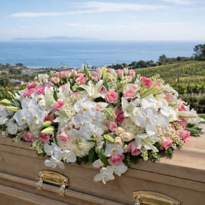 White and pink floral casket spray on a wooden casket