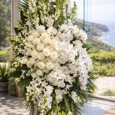 Tall white floral arrangement with roses and orchids on an easel