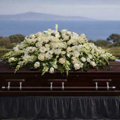 White floral casket spray on a dark wood coffin outdoors