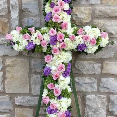 Floral cross arrangement with pink roses, white hydrangeas, and purple blooms