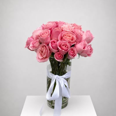Pink roses arranged in a clear glass vase with a white ribbon