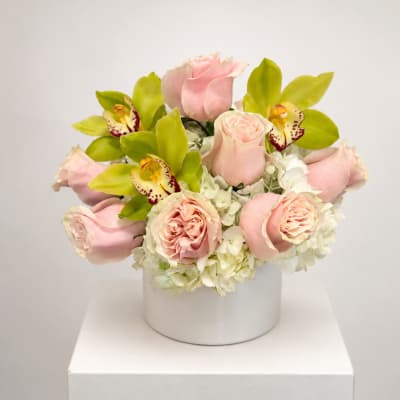 Pink roses and green orchids arranged in a white box vase