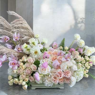 Large pastel floral arrangement with roses, orchids, and white blooms in a low container