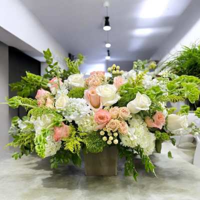 Large floral arrangement with white and blush roses in a square vase