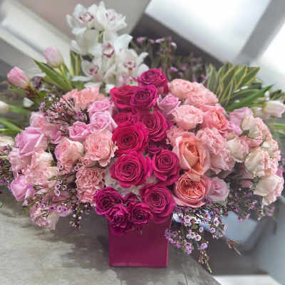 Pink and white rose arrangement in a magenta vase with orchids