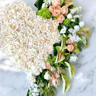 Heart-shaped floral arrangement of white and peach roses with green accents