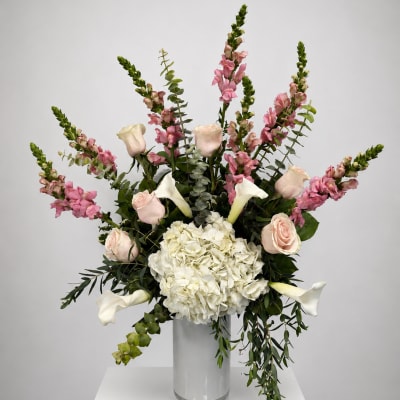 Tall vase arrangement with white hydrangea, pale roses, pink snapdragons, and white calla lilies