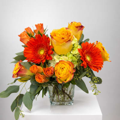 Orange and yellow roses with red gerbera daisies in a glass vase