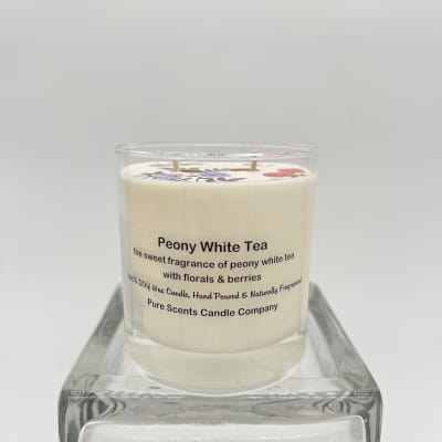 White scented candle labeled Peony White Tea in a clear glass jar on a glass stand