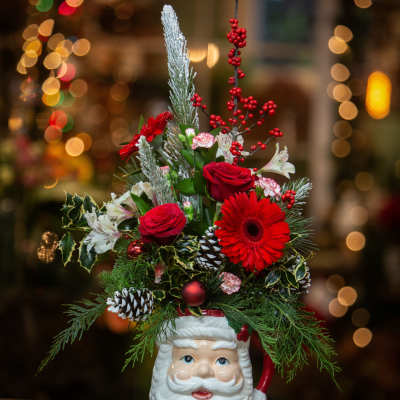 Christmas arrangement in a Santa-face mug with red flowers and pinecones